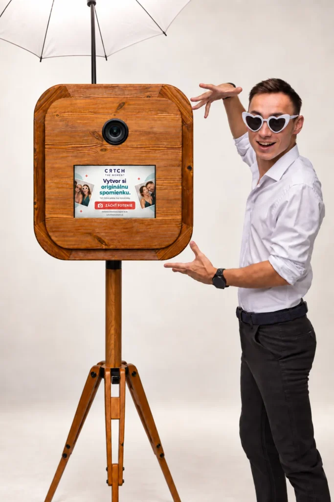 Operátor vo vtipných okuliaroch ukazuje na dotykovú obrazovku fotobúdky so štúdiovým dáždnikom